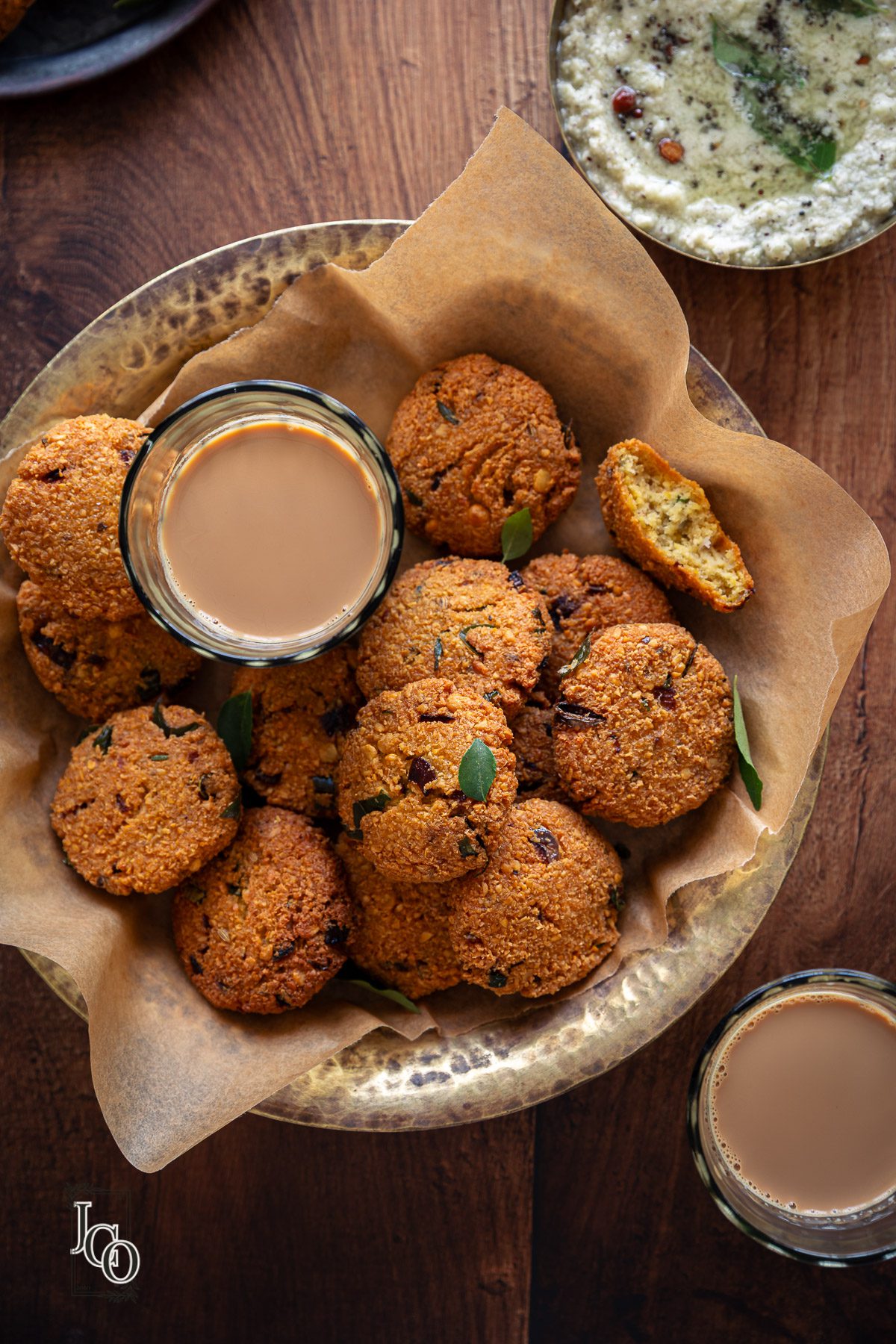 chana dal vada in a serving bowl on parchment paper, served with tea and coconut chutney.