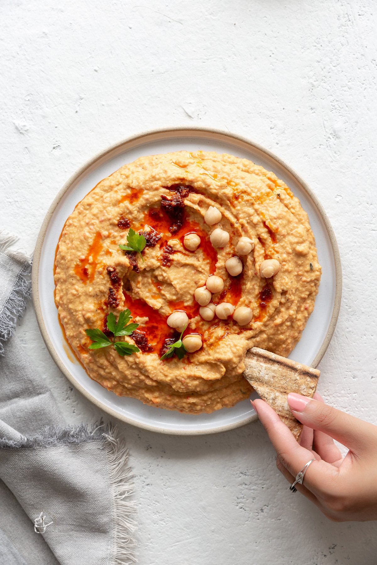 A female hand is dipping a pitta bread chips in roasted red pepper hummus