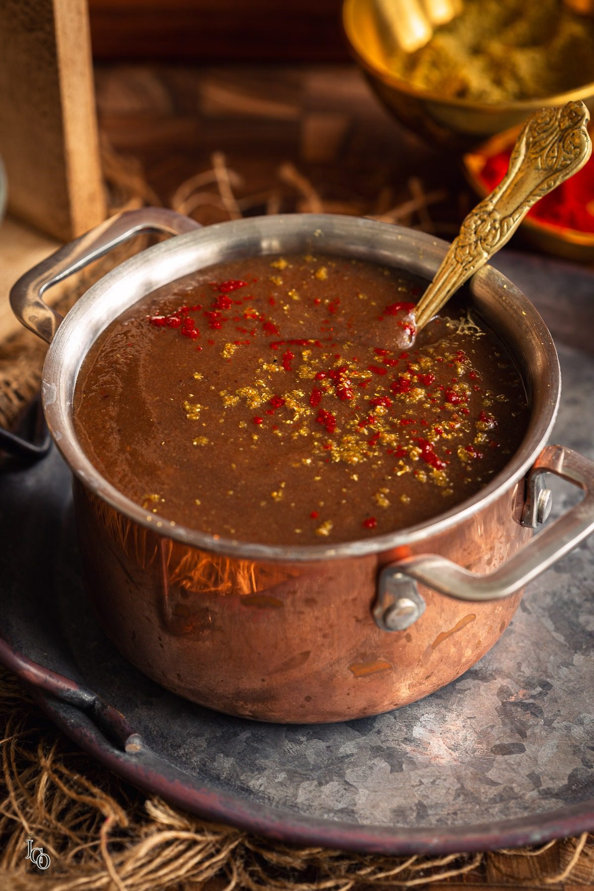 A bowl of chutney with a spoon inside placed on a round metal tray.
