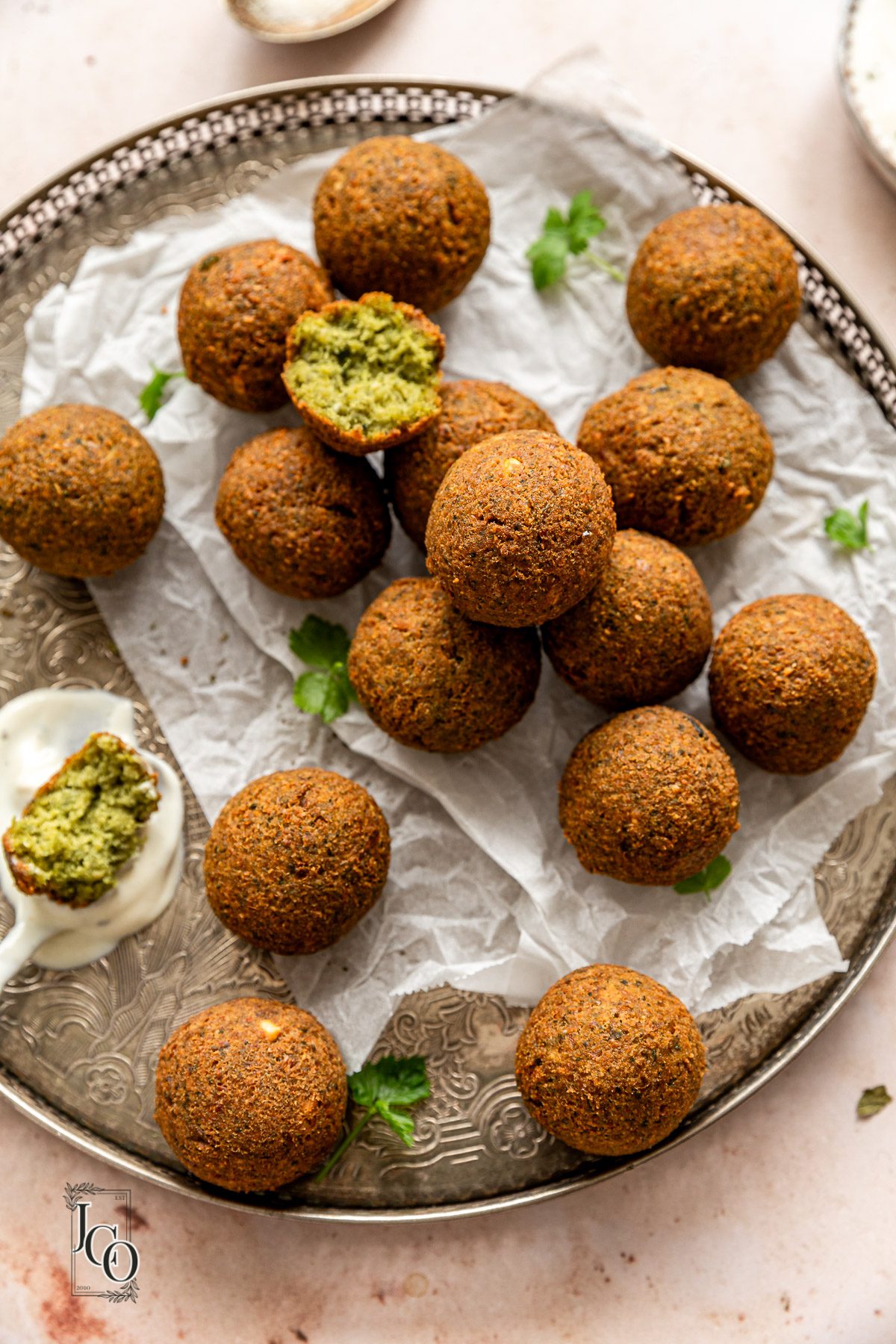 A plate full of deepfried falafels placed on the table next to a sauce bowl.