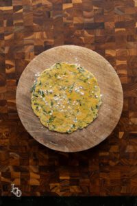 Uncooked rolled methi paratha on a surface.