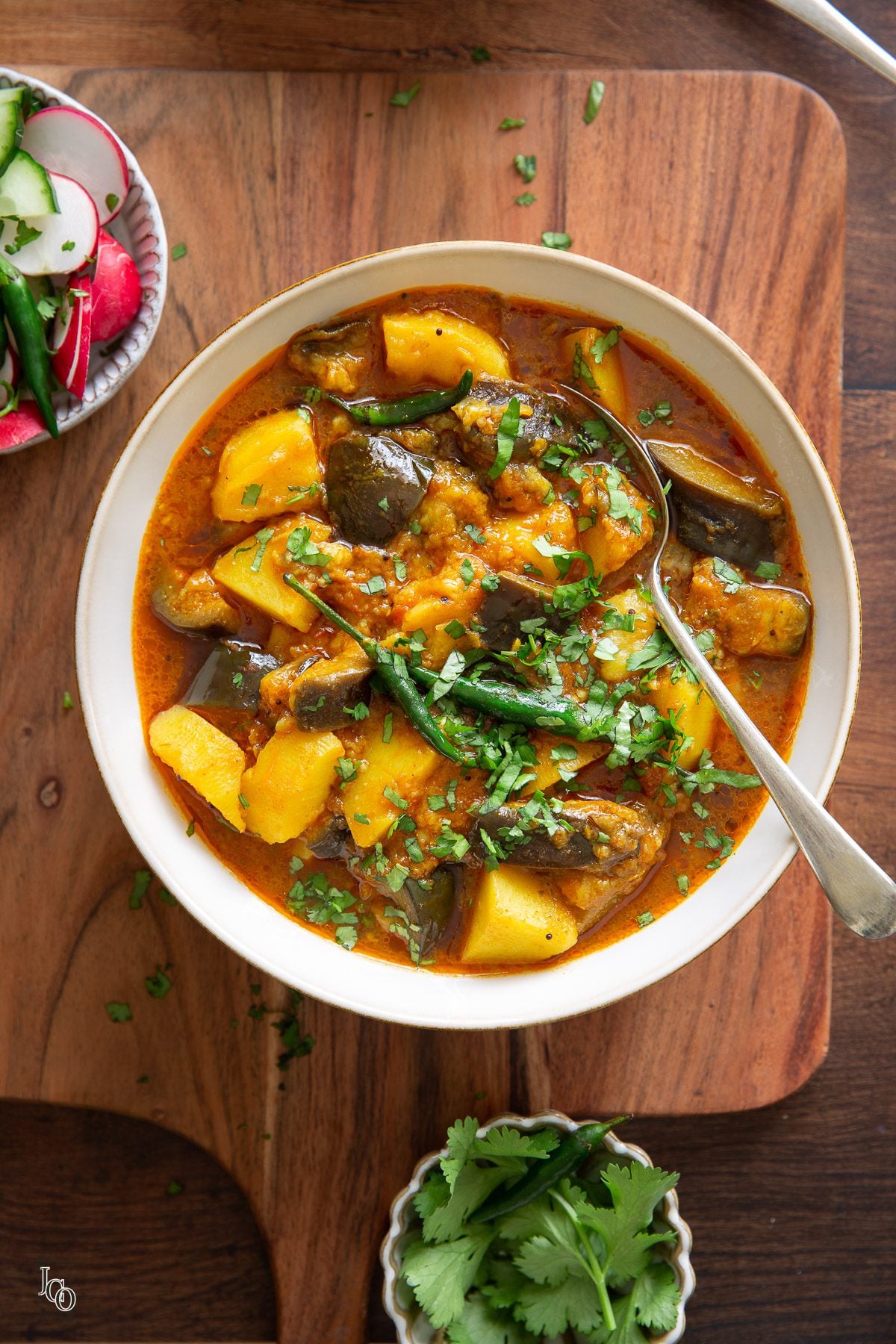 potatoes and aubergines in a tomato based gravy served in a bowl and garnished with coriander. 
