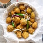 Deep fried fritters served on parchment paper with green chillies, onion slices and tea.