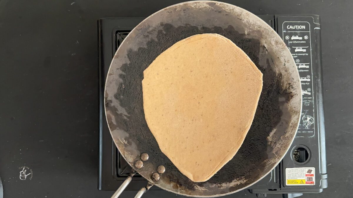 uncooked paratha on a hot griddle on stove top.