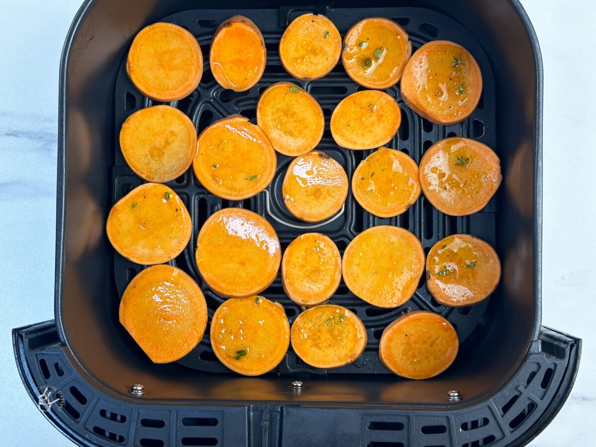 thinly cut sweet potatoes slices are arranged in the air fryer basket