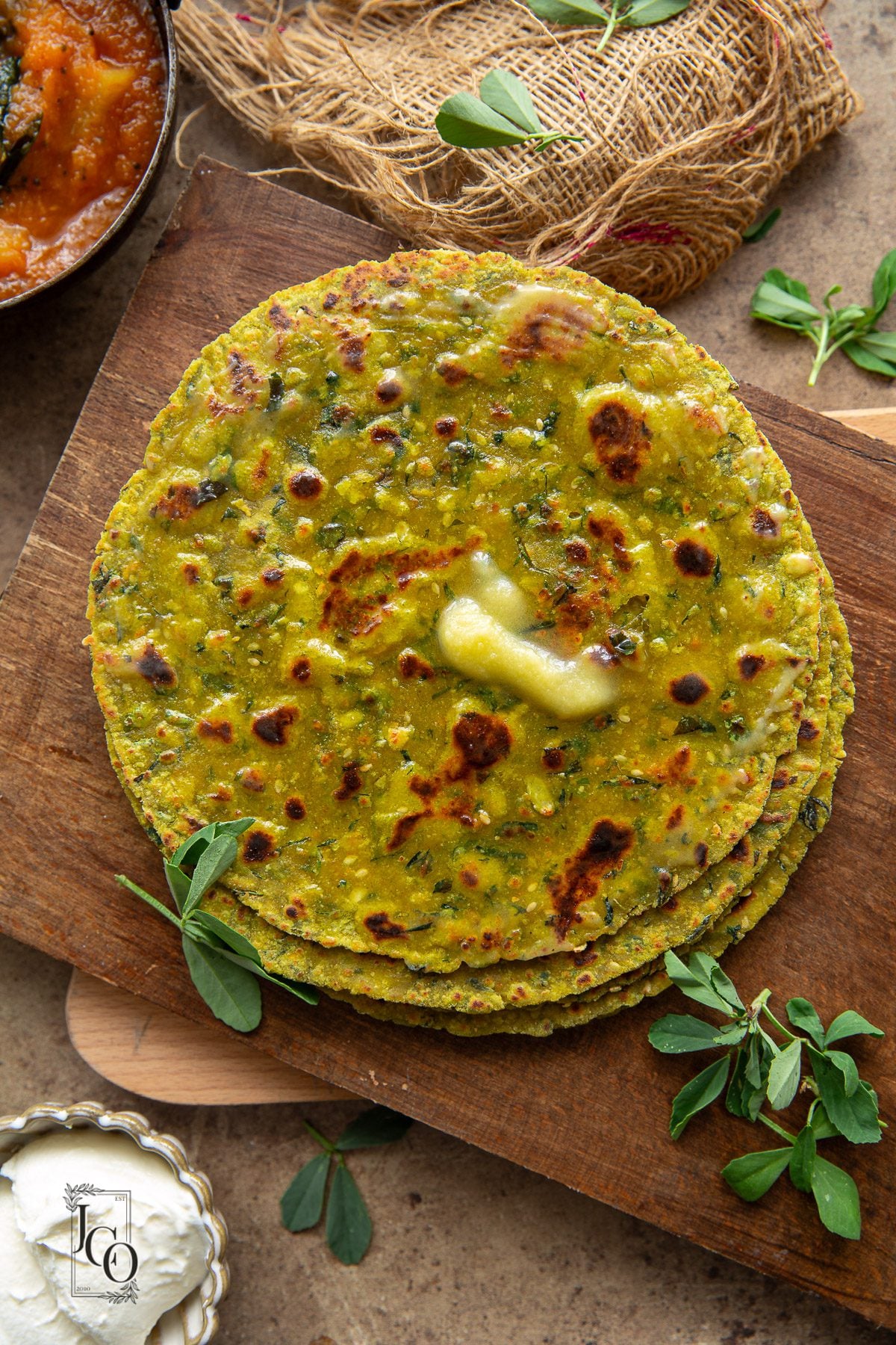 A stack of savoury Indian flatbreads are on a serving board.