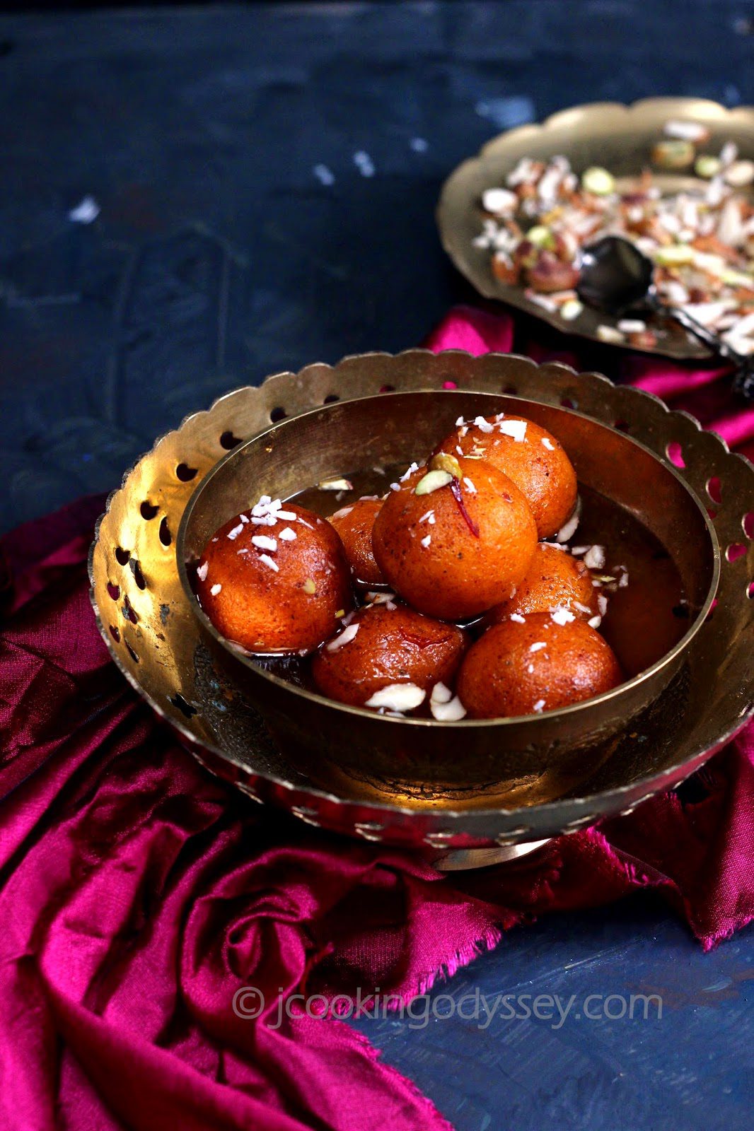 a gold bowl filled with sweet potato jamun garnished with nuts. placed on a royal pink cloth