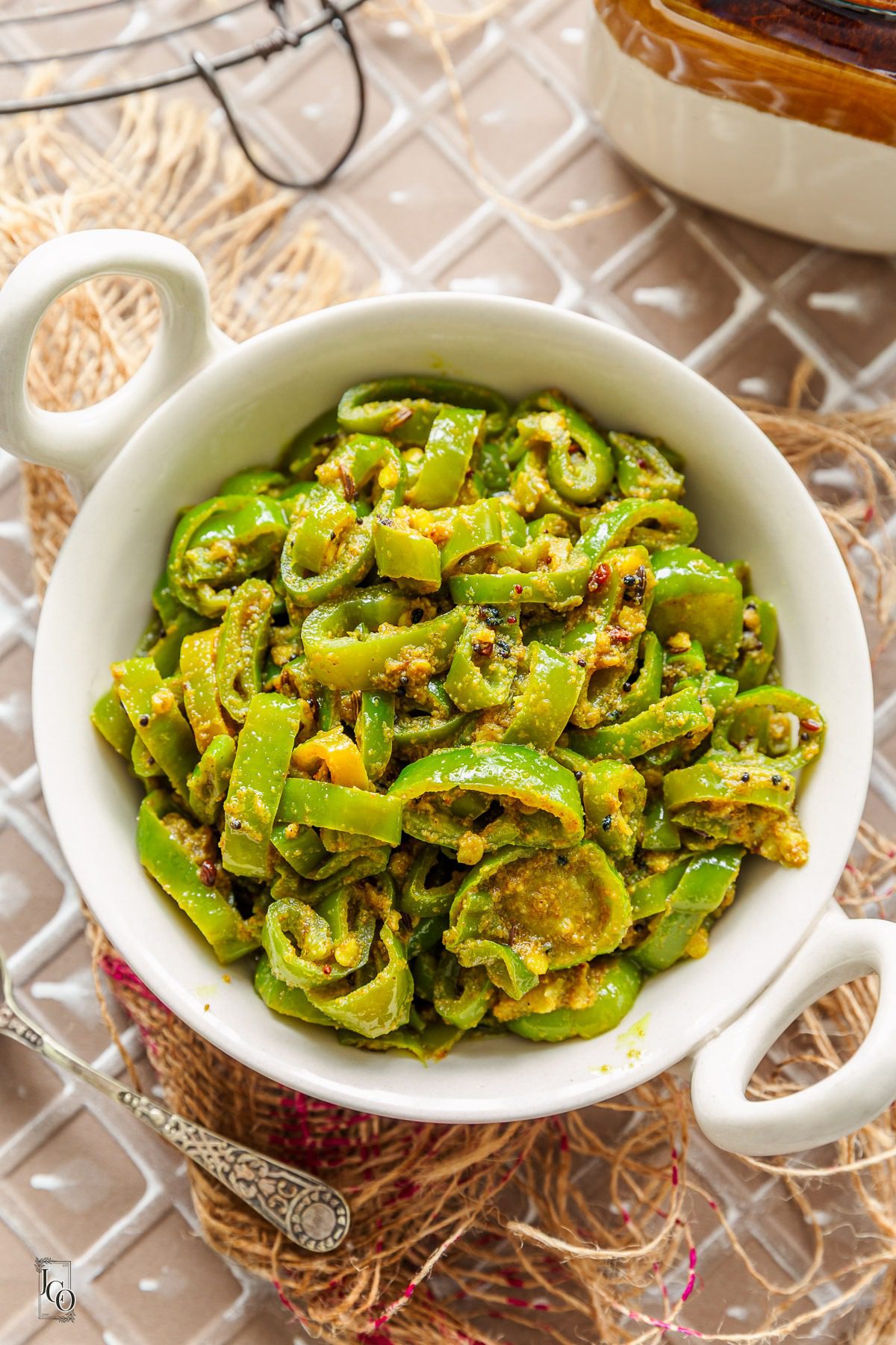 A small bowl of green chilli pickle placed on a jute piece next to a small spoon.
