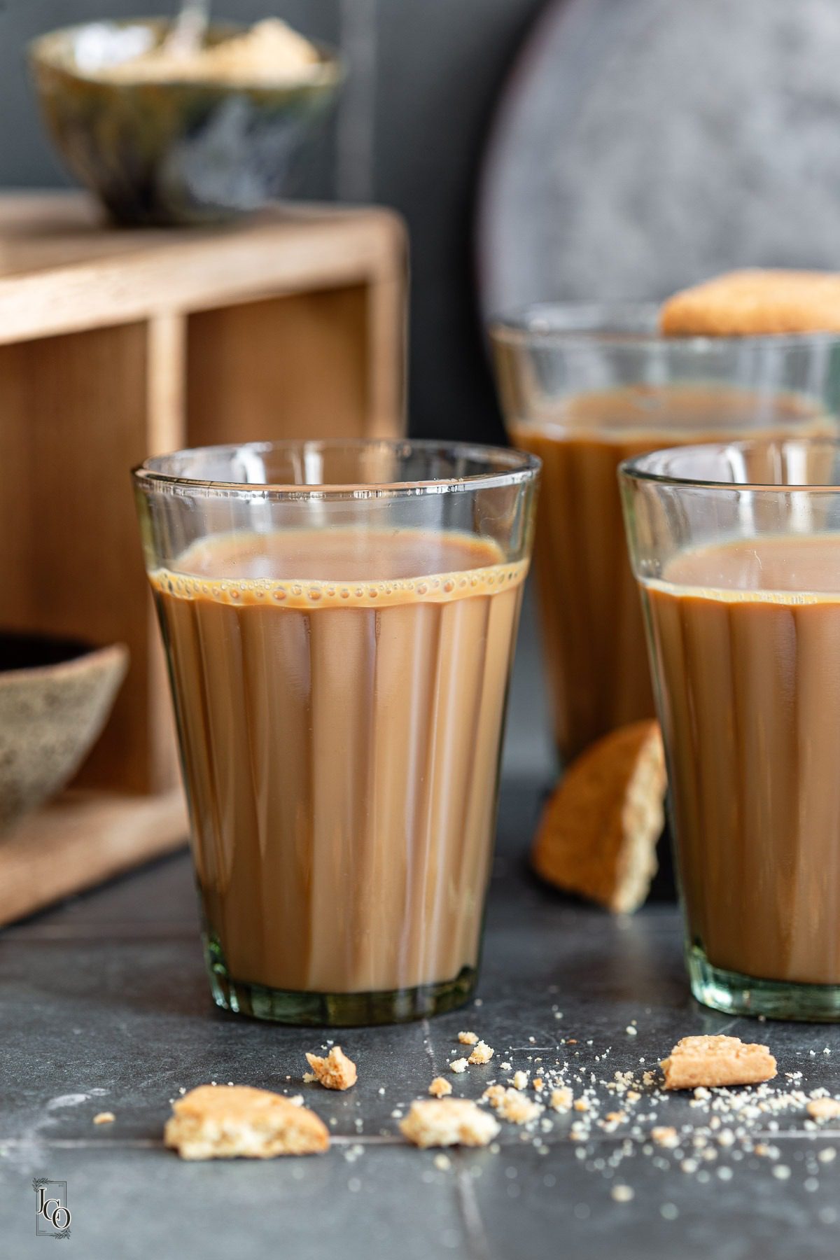 Masala chai cups placed on a table, some cookie crumbs in the foreground.