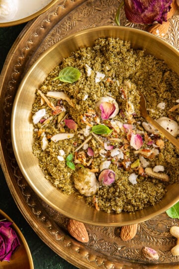 A bowl of dhaniya panjiri placed next to dried pink roses.