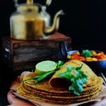 stack of paratha served on a wooden board. an old tea kettle in the background