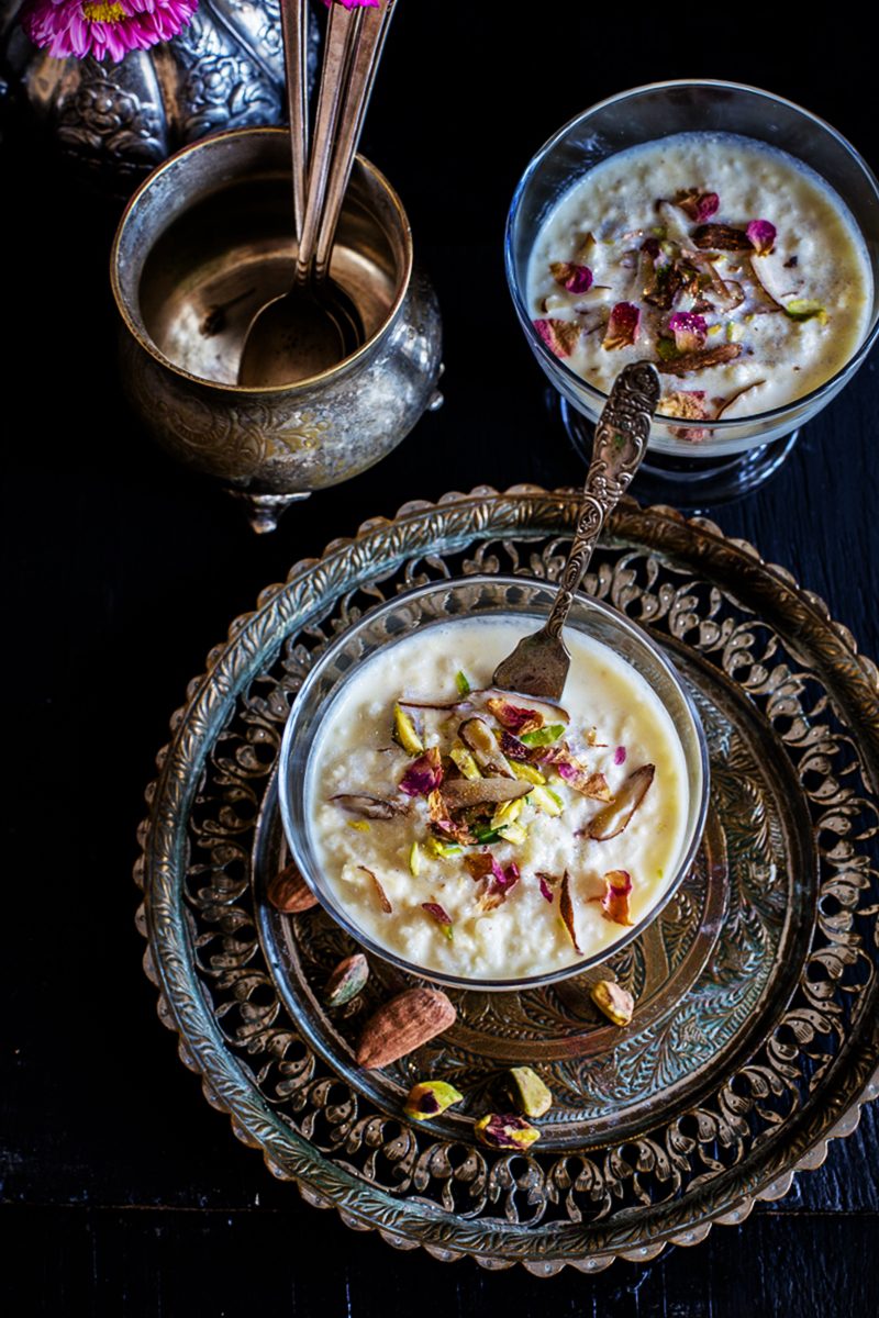 a decorative bowl filled with paneer doodh poha topped with rose petals and nuts