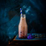 a glass bottle filled with blueberry smoothie against a blue background