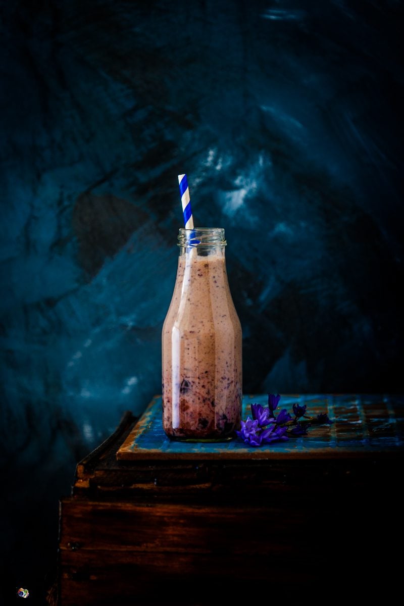 a glass bottle filled with blueberry smoothie against a blue background