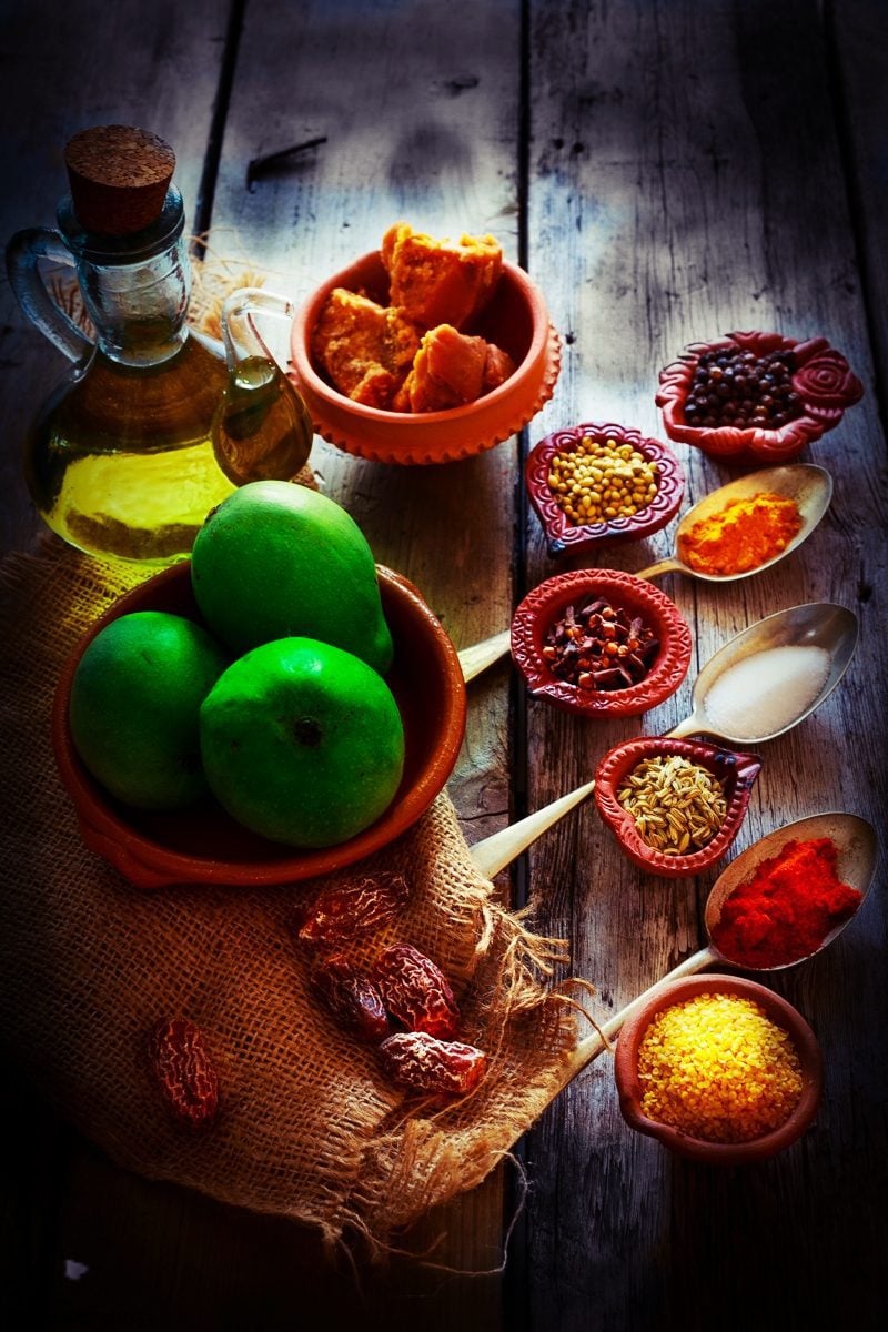 Gor keri pickle ingredients raw mangoes, oil, spices and jaggery placed on the kitchen worktop.