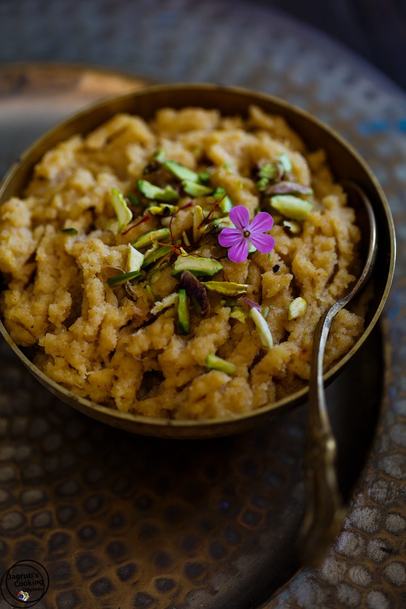 a dark bowl filled with pineapple and coconut halwa and topped with pistachio slivers