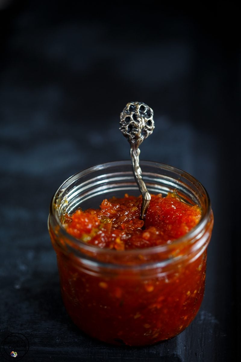 a glass jar filled with red pepper chutney with a decorative spoon to serve