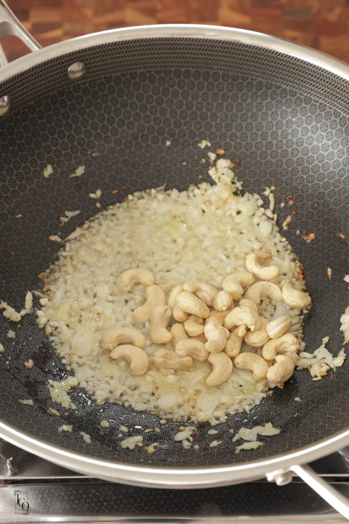 Cashew nuts added to sauteed onions in a pan.