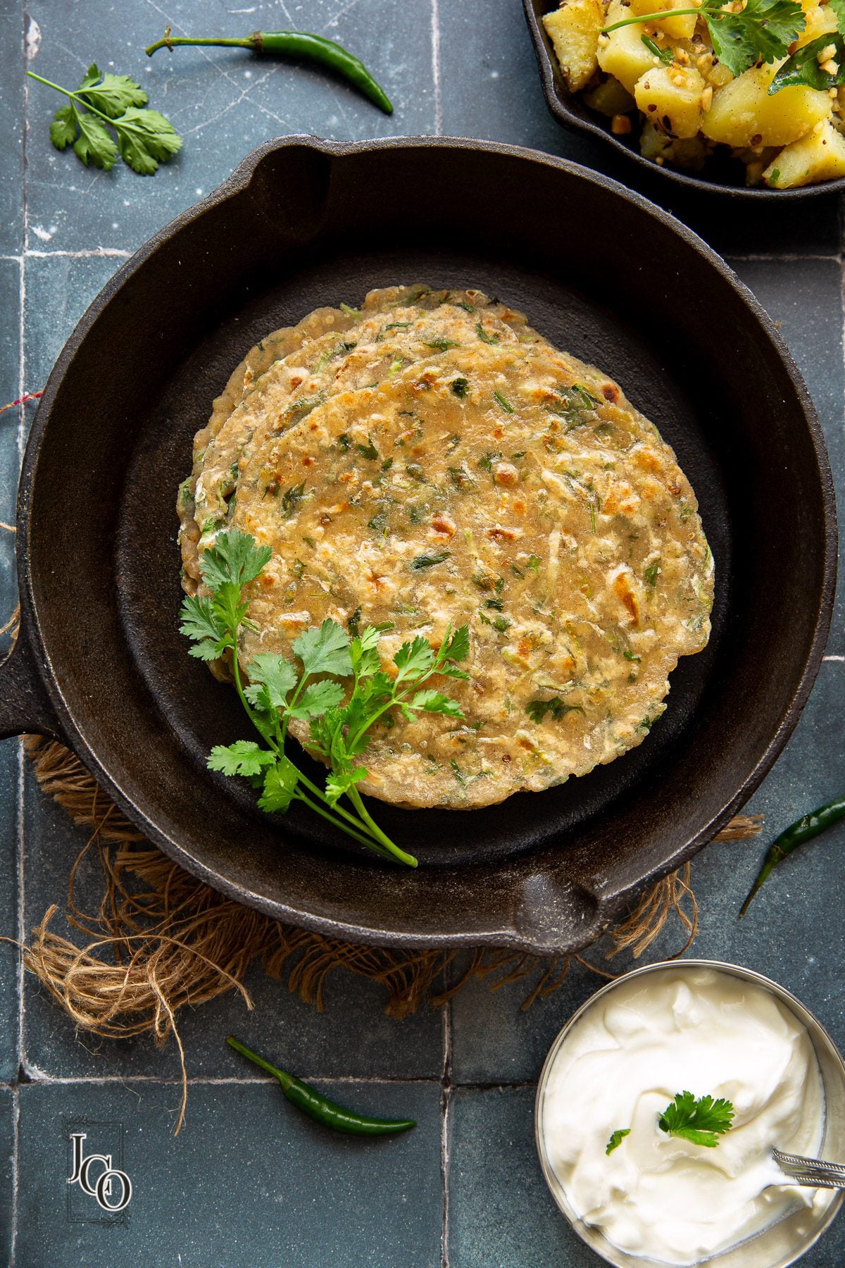 A few leaves of coriander placed near pan fried indian flatbreads on a griddle.
