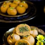 Stuffed magas ladoo placed on a brass plate next to half cut ladoo showing pistachio filling