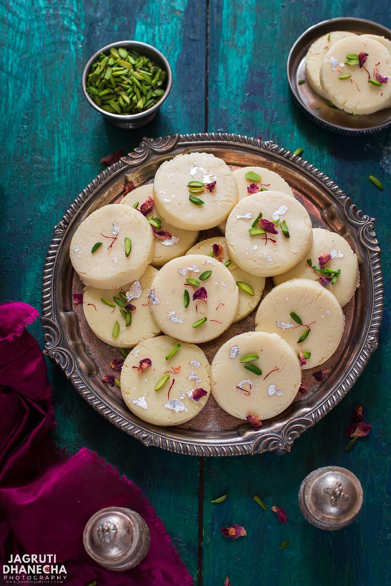 Rajkot na peda served in a silver metal plate and garnished with slivered pistachios and rose petals