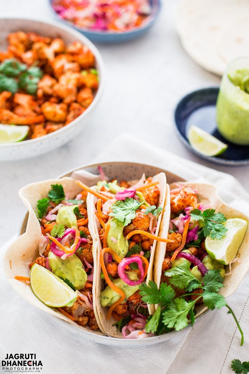 Tandoori cauliflower and chickpea tacos are served in a white round bowl and garnished with freshly chopped cilantro and avocado cream