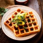 Two waffle idli delights placed on a cream colour plate and topped with spicy potato mixture with chutney