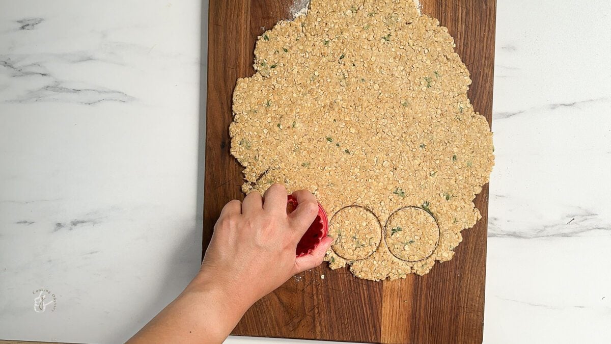 female hand is cutting rounds from oatcakes dough using a cookie cutter