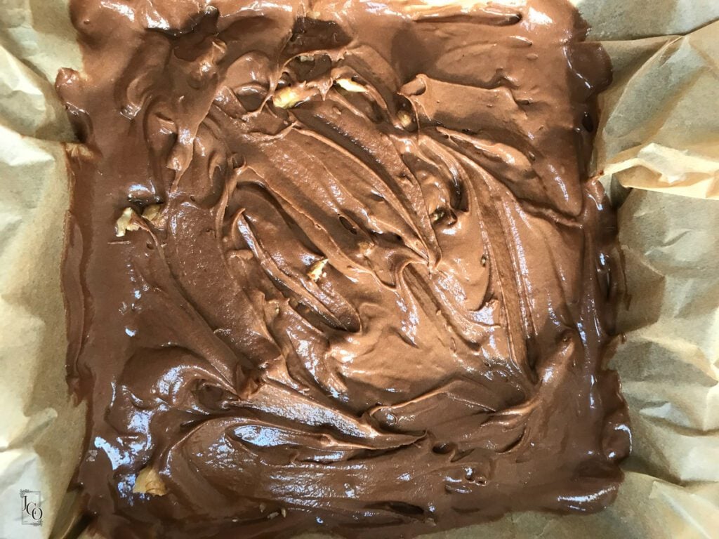 Brownie batter in a baking tray. Chopped walnuts sprinkled over it.