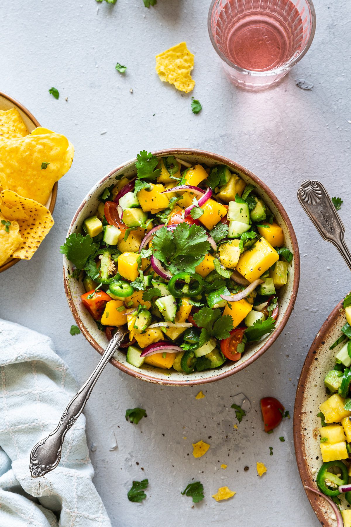 Mango avocado salsa with passionfruit srved in two bowls with tortilla chips and drinks on the side.