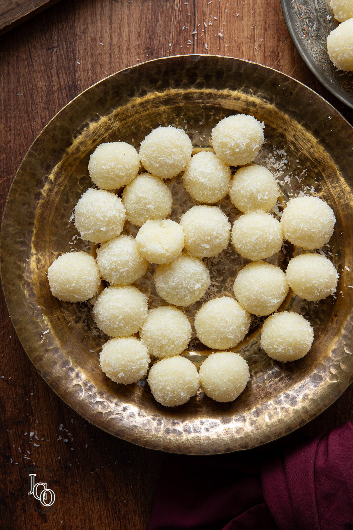 Coconut ladoo arranged in a serving bowl, next to a small plate and purple napkin.