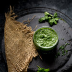 Green mint and coriander chutney placed in a small glass jar on a black slate tile