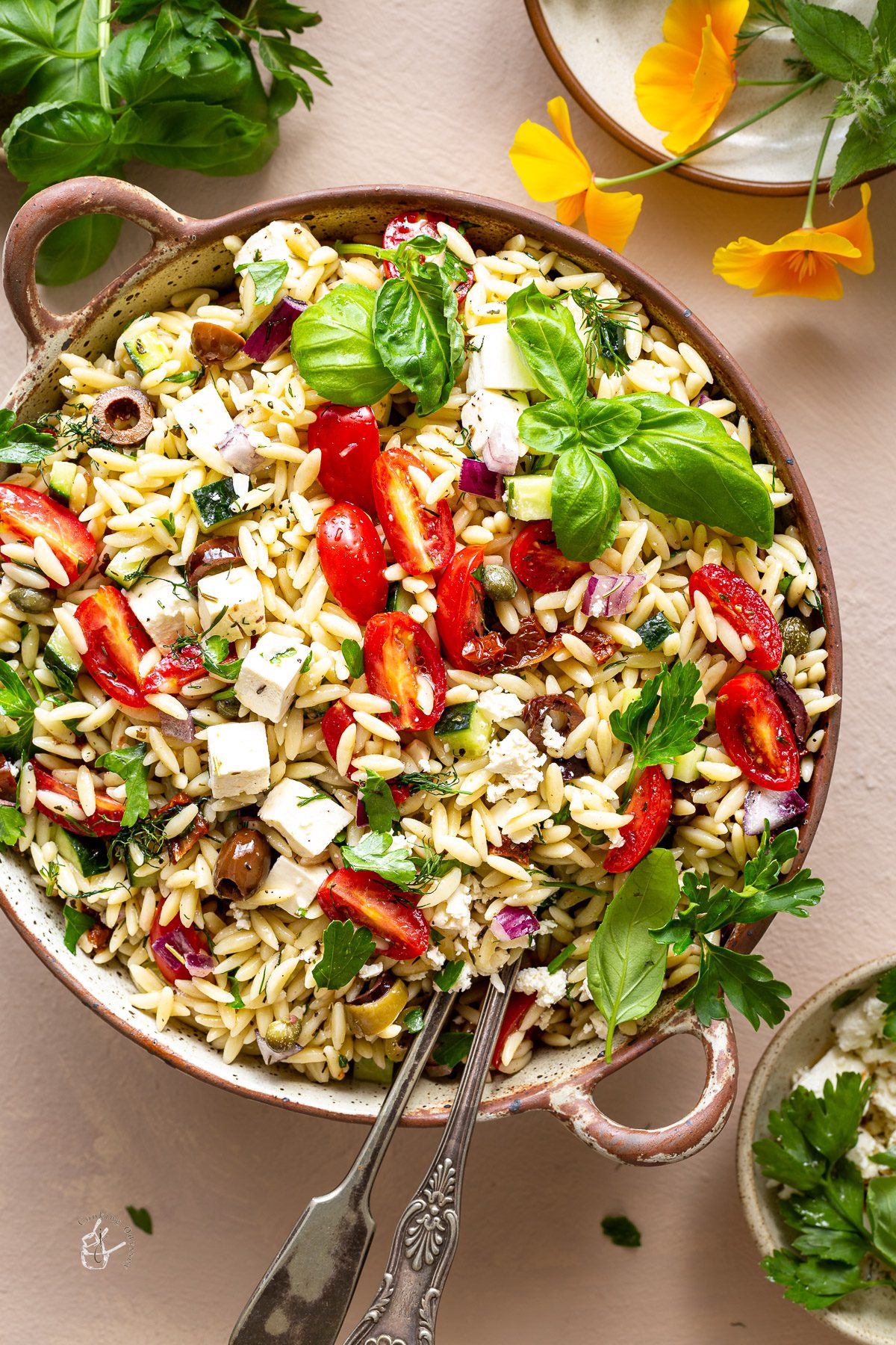 Pasta salad served in a bowl with two serving spoons.