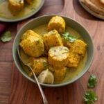 Creamy coconut and sweetcorn curry in a bowl next to a plate of rotis.