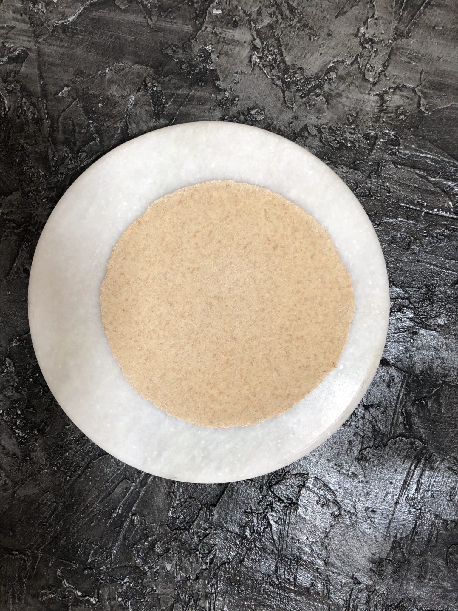 Uncooked round rolled chapati on a round marble slab. 