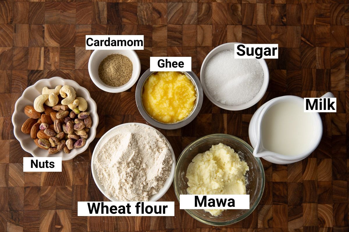 Whole wheat flour, ghee, mawa, sugar and nuts in small bowls.