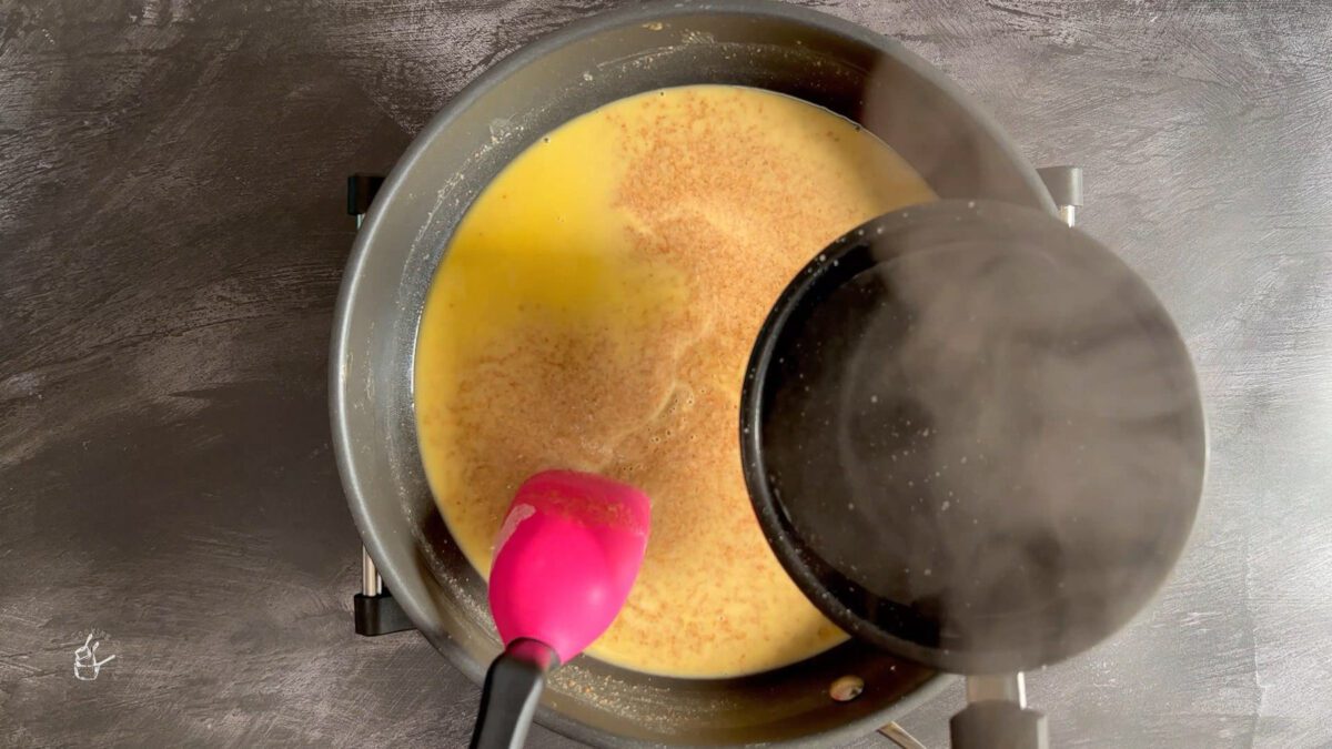 a female hand is pouring hot water in to the roasted mixture for wheat halwa