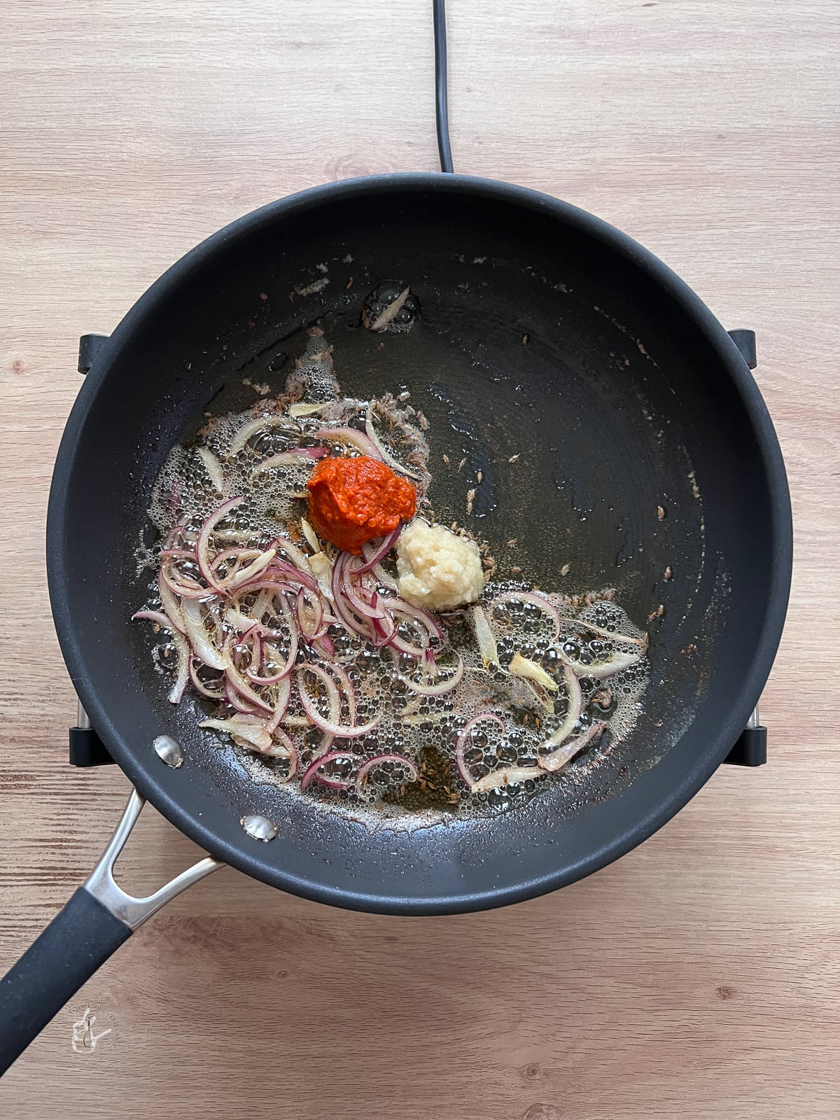 Onion slices cooking in oil in a pan with garlic and chilli paste. 