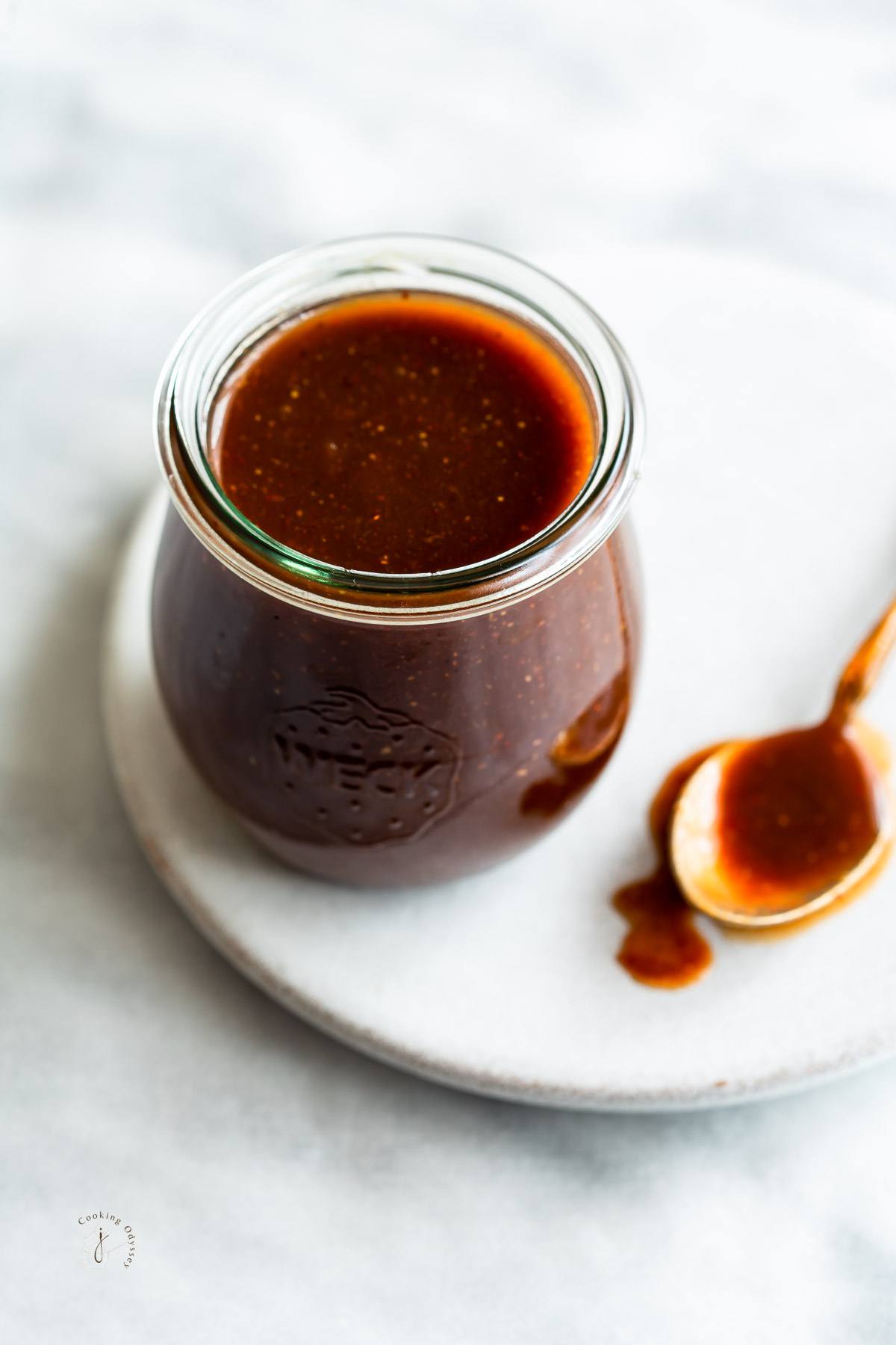 a jar of tamarind sauce is placed on a white round slab with a spoon on the side