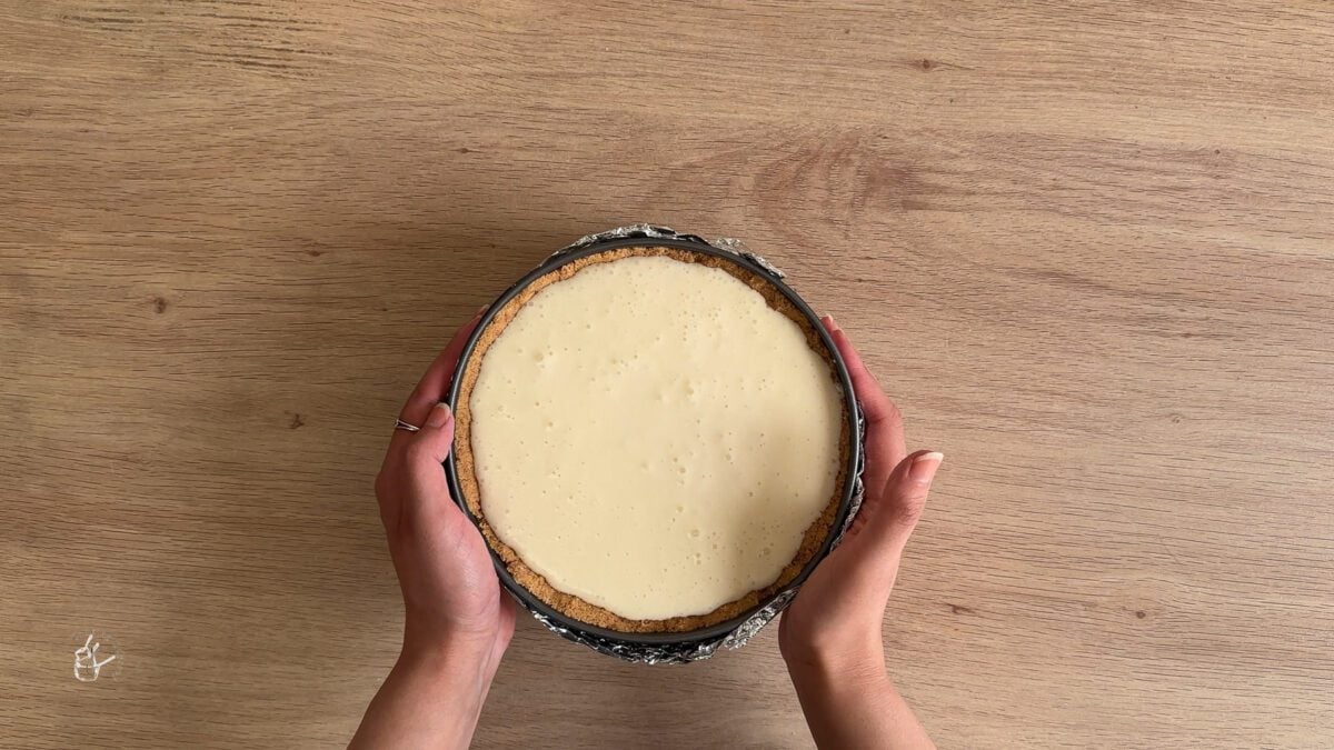 a female hand is tapping cheesecake tin on the board to remove bubbles from the filling