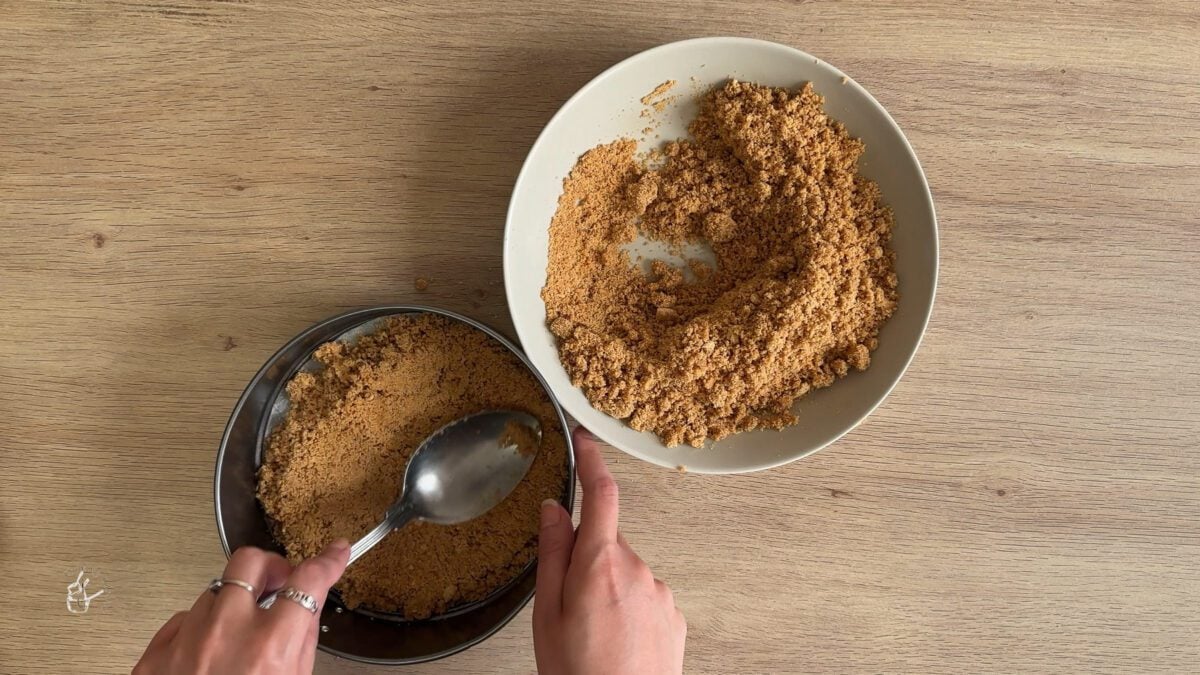a female hand is setting a cheesecake base in a cake tin
