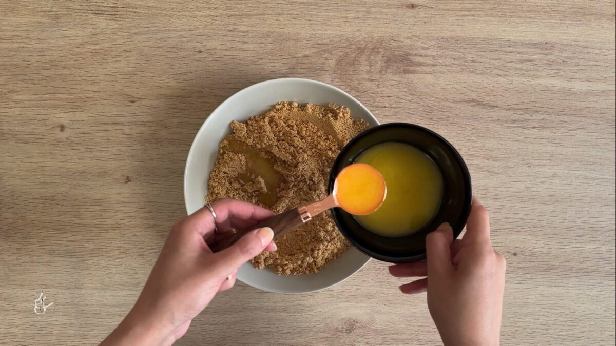 a female hand is pouring melted butter in crushed biscuits