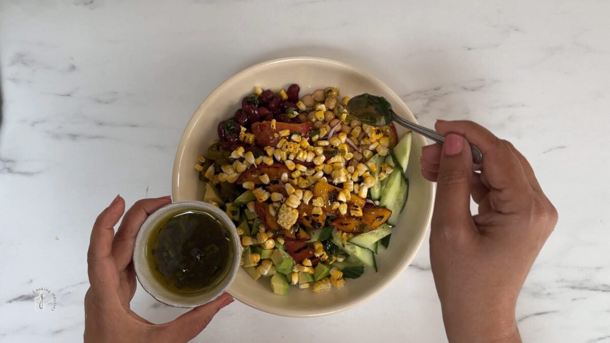 a female hand is drizzling dressing on the salad