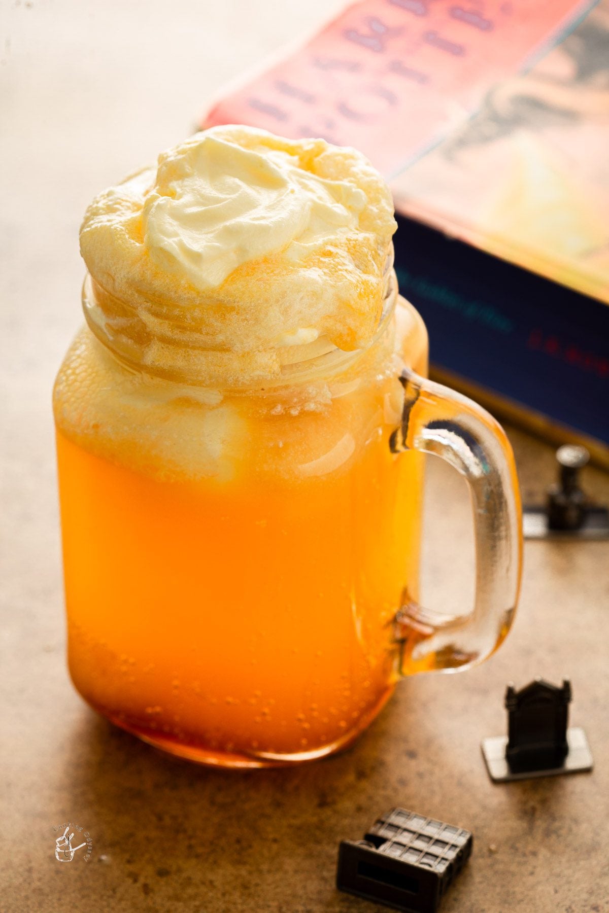 a glass of homemade butter beer placed next to harry potter book - how to make butterbeer