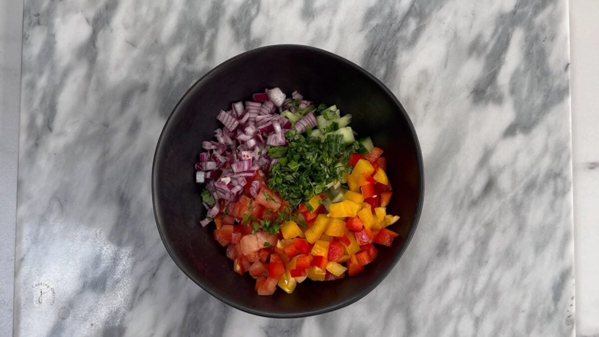 israeli salad in a bowl topped with chopped herbs and dressing 