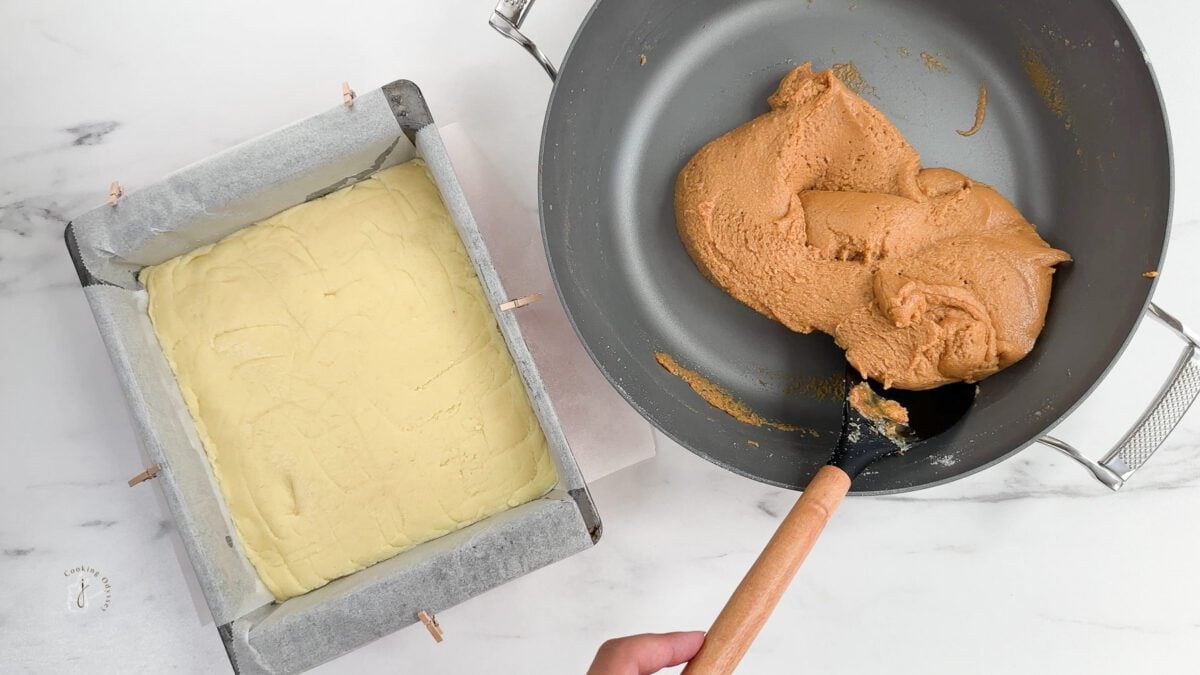 A female hand is spreading caramel barfi mixture  on the layers vanilla barfi 