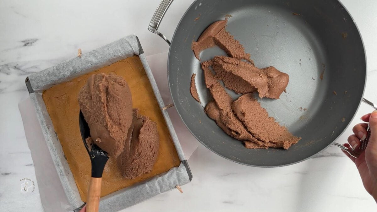 a female hand is spreading chocolate barfi mixture in the tray