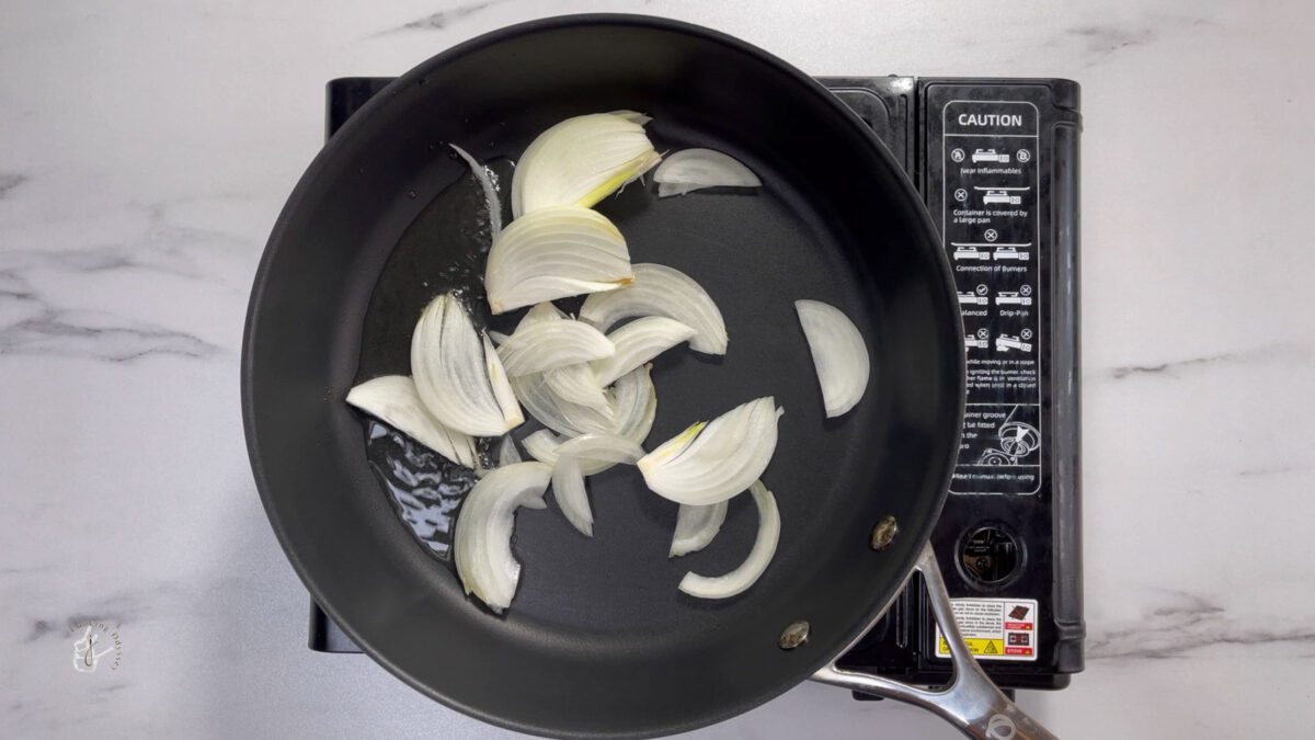 sliced onions added to the hot oil in a pan