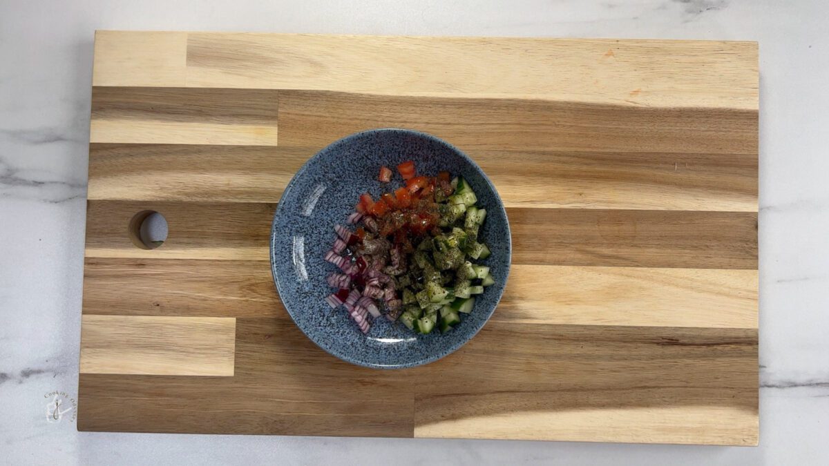 dried mint sprinkled on chopped vegetables in blue bowl