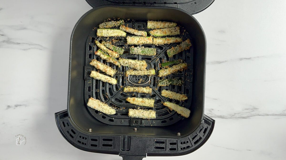 Cooked air fryer zucchini fries in the air fryer basket on a kitchen worktop